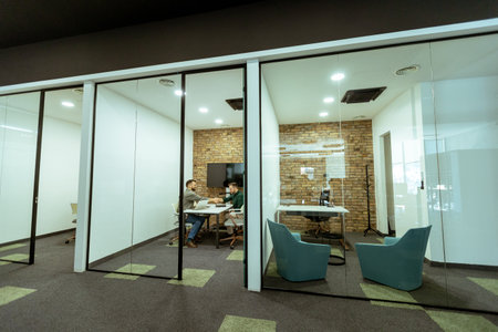 Two professionals engage in a conversation while seated comfortably in an office lounge, surrounded by greenery and contemporary design elementsの写真素材