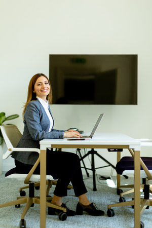 A businesswoman exudes confidence as she works on her laptop, seated at a modern desk in a well-lit room.の写真素材