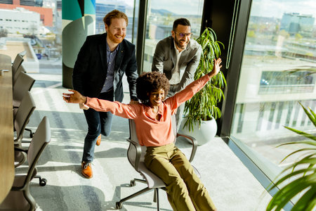 Exuberant co-workers engage in an impromptu office chair race, basking in the afternoon light with laughter.の写真素材