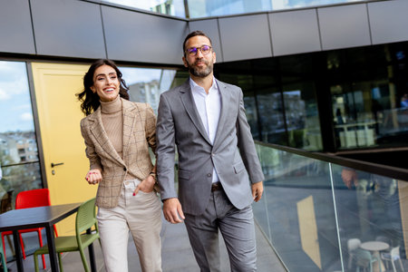 Two professionals exude confidence and happiness as they walk out of a contemporary office, reflecting success.の写真素材