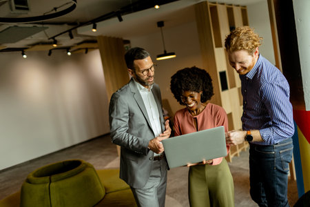 Three colleagues laugh and discuss ideas around a laptop in a vibrant, modern workspace