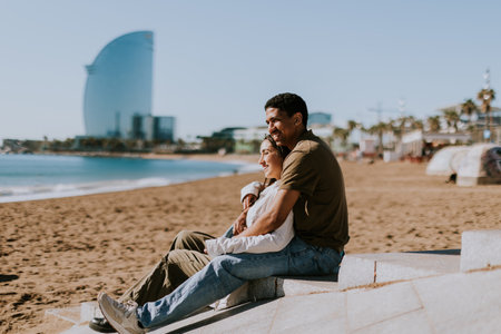Couple relaxes on Barcelonas sandy shores, with the iconic hotel in the backdropの写真素材