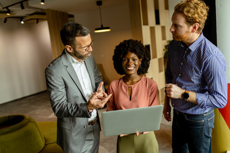 Three colleagues laugh and discuss ideas around a laptop in a vibrant, modern workspaceの写真素材