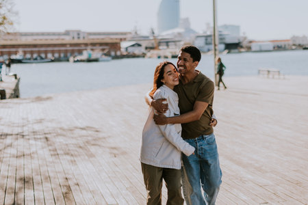 Joyful couple hugs on a pier in Barcelona, with the city skyline softly blurred in the backgroundの写真素材