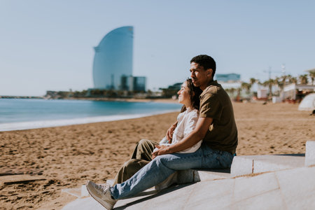 Couple relaxes on Barcelonas sandy shores, with the iconic hotel in the backdropの写真素材