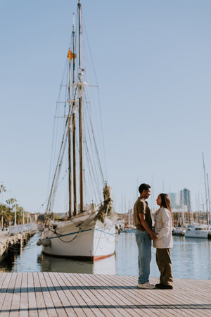 Cuple enjoys a peaceful walk beside moored boats in Barcelona tranquil marina, basking in the soft morning light.の写真素材