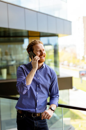 A focused man in a striped shirt talks on his phone while overlooking the balcony at bathed in sunlight.の写真素材