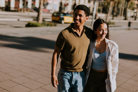 Young couple holds hands and smiles as they walk down a sunlit path in Barcelona, framed by palmsの写真素材