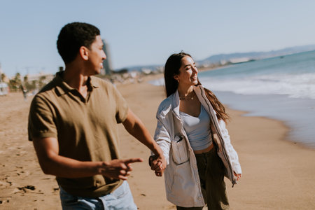 A smiling couple enjoys a carefree run on a sandy shore, waves gently breaking in the backgroundの写真素材