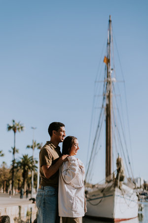 Young couple embraces while exploring the enchanting seaside atmosphere of Barcelonas marina