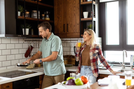 A man and woman sharing a laugh as they cook in a cozy, well-organized kitchenの写真素材