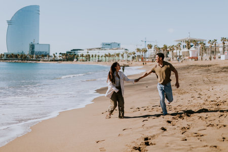 A smiling couple enjoys a carefree run on a sandy shore, waves gently breaking in the backgroundの写真素材