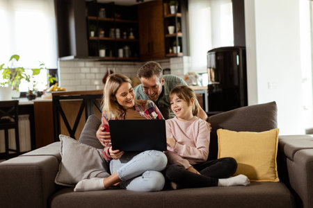 Joyful family of three spends quality time together on the living room sofa, sharing a moment around a laptop in their comfortable homeの写真素材