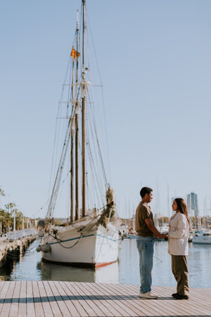 Cuple enjoys a peaceful walk beside moored boats in Barcelona tranquil marina, basking in the soft morning light.の写真素材