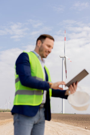 A professional with a tablet smiles optimistically at a wind farmの写真素材