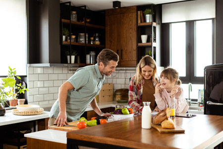 Young family chatting and preparing food around a bustling kitchen counter filled with fresh ingredients and cooking utensilsの写真素材