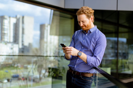 A focused man in a striped shirt talks on his phone while overlooking the balcony at bathed in sunlight.の写真素材
