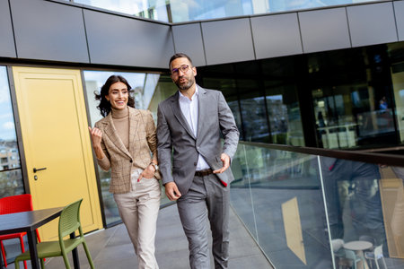 Two professionals exude confidence and happiness as they walk out of a contemporary office, reflecting success.の写真素材
