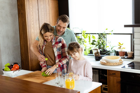 Young family chatting and preparing food around a bustling kitchen counter filled with fresh ingredients and cooking utensilsの写真素材