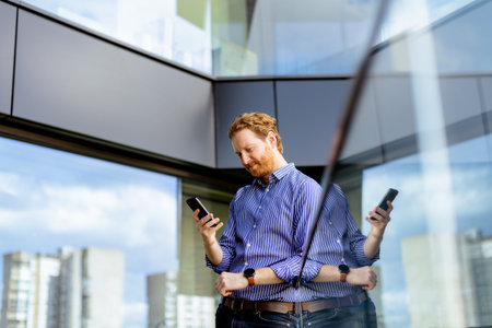 A focused man in a striped shirt talks on his phone while overlooking the balcony at bathed in sunlight.の写真素材