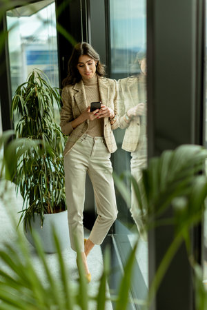 Stylish lady gazes out a window, holding a smartphone, amidst the urban allureの写真素材