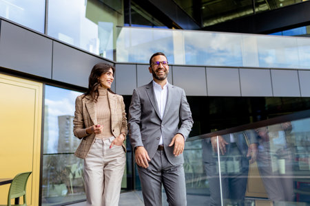 Two professionals exude confidence and happiness as they walk out of a contemporary office, reflecting success.の写真素材