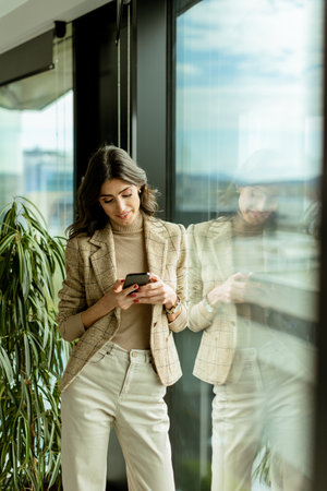 Stylish lady gazes out a window, holding a smartphone, amidst the urban allureの写真素材