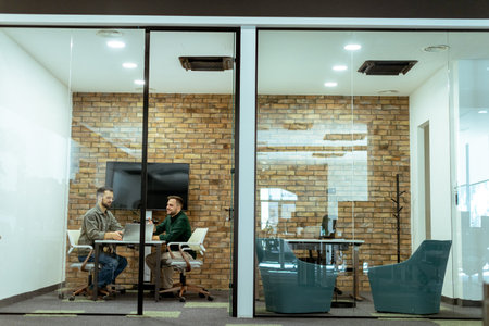 Two professionals engage in a conversation while seated comfortably in an office lounge, surrounded by greenery and contemporary design elementsの写真素材