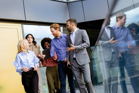 Group of colleagues in a casual business huddle, sharing ideas next to a reflective glass facade as the day ends.の写真素材