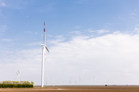 Wind turbines stand tall against a vast horizon, with a solitary tree contrasting the arid terrain.の写真素材