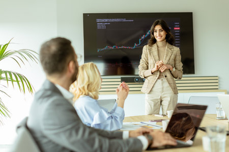 Businesswoman points at growth trends on a screen during a financial meeting, with attendees listening intentlyの写真素材