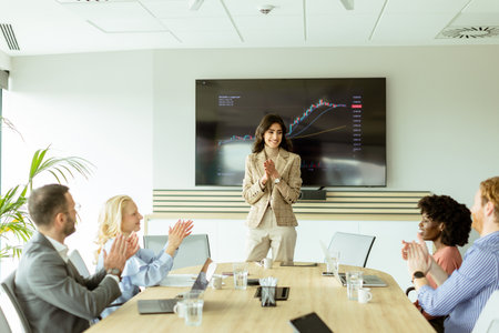 Businesswoman points at growth trends on a screen during a financial meeting, with attendees...