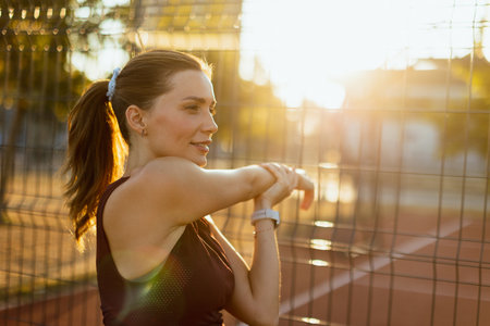 As the sun begins to set, a focused female athlete engages in a stretching routine on the court, soaking in the vibrant colors of the sunset while preparing for her practice.の写真素材