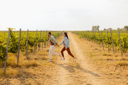 Young couple enjoys a carefree moment as they run through rows of verdant grapevines, basking in the warm sunlight of an idyllic afternoon in the vineyardの写真素材