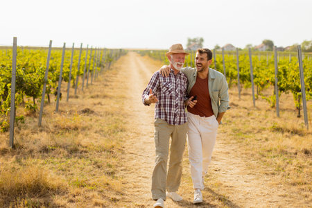 Walking along a dusty path in a sunny vineyard, two men engage in lighthearted conversation, their camaraderie evident against the backdrop of sprawling grapevinesの写真素材