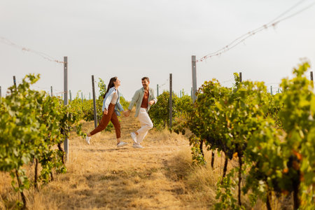 Young couple enjoys a carefree moment as they run through rows of verdant grapevines, basking in the warm sunlight of an idyllic afternoon in the vineyardの写真素材