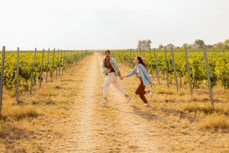 Young couple enjoys a carefree moment as they run through rows of verdant grapevines, basking in the warm sunlight of an idyllic afternoon in the vineyardの写真素材