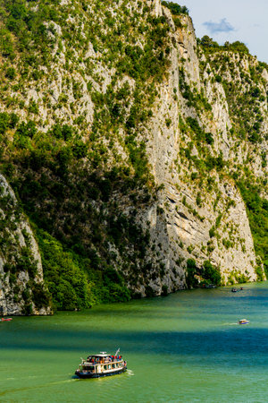 Boat glides through the serene waters of the Danube, surrounded by magnificent cliffs and lush greenery in the captivating Djerdap Gorge, Serbiaâs natural wonderの写真素材