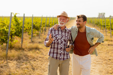 Walking along a dusty path in a sunny vineyard, two men engage in lighthearted conversation, their camaraderie evident against the backdrop of sprawling grapevinesの写真素材