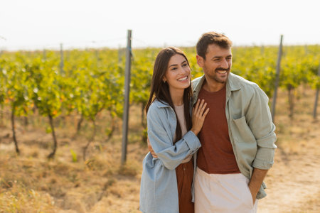 As they walk together, the couple enjoys the tranquility of the vineyards, surrounded by rows of green vines under a clear sky on a warm afternoonの写真素材