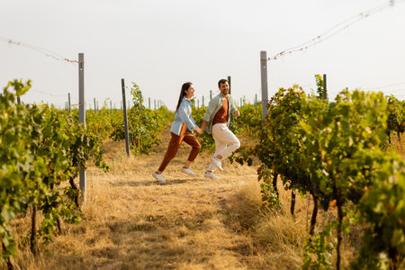 Young couple enjoys a carefree moment as they run through rows of verdant grapevines, basking in the warm sunlight of an idyllic afternoon in the vineyardの写真素材