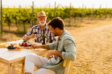 Two friends savor the rich flavors of local wine and delicious snacks at a rustic outdoor table, basking in the golden glow of the vineyard at sunsetの写真素材