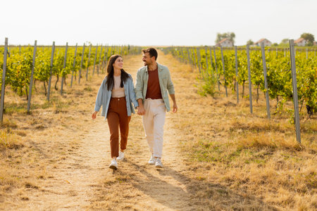 As they walk together, the couple enjoys the tranquility of the vineyards, surrounded by rows of green vines under a clear sky on a warm afternoonの写真素材