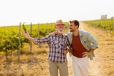 Walking along a dusty path in a sunny vineyard, two men engage in lighthearted conversation, their camaraderie evident against the backdrop of sprawling grapevinesの写真素材