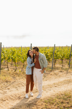 As they walk together, the couple enjoys the tranquility of the vineyards, surrounded by rows of green vines under a clear sky on a warm afternoonの写真素材