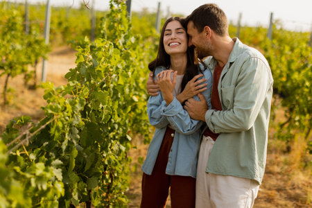 Young couple shares a joyful moment among verdant vines, laughing and embracing under the warm sun, celebrating love and the serenity of a picturesque vineyardの写真素材