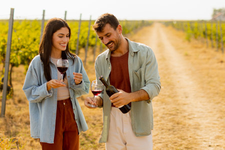 Under the warm glow of the setting sun, a couple shares laughter while sipping wine in a picturesque vineyard, creating cherished memories amid rows of grapevinesの写真素材