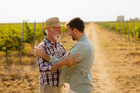 Amidst the lush rows of grapevines, a joyous embrace unfolds between two generations, capturing a moment of love and connection on a sunny dayの写真素材