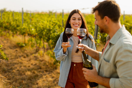 Under the warm glow of the setting sun, a couple shares laughter while sipping wine in a picturesque vineyard, creating cherished memories amid rows of grapevinesの写真素材