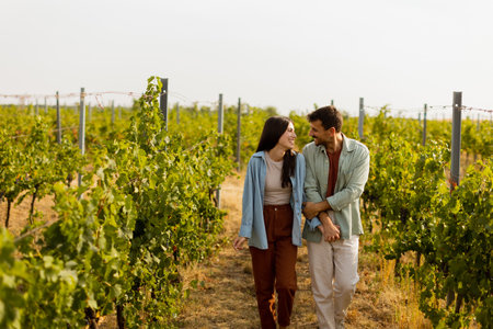 Young couple shares a joyful moment among verdant vines, laughing and embracing under the warm sun, celebrating love and the serenity of a picturesque vineyardの写真素材